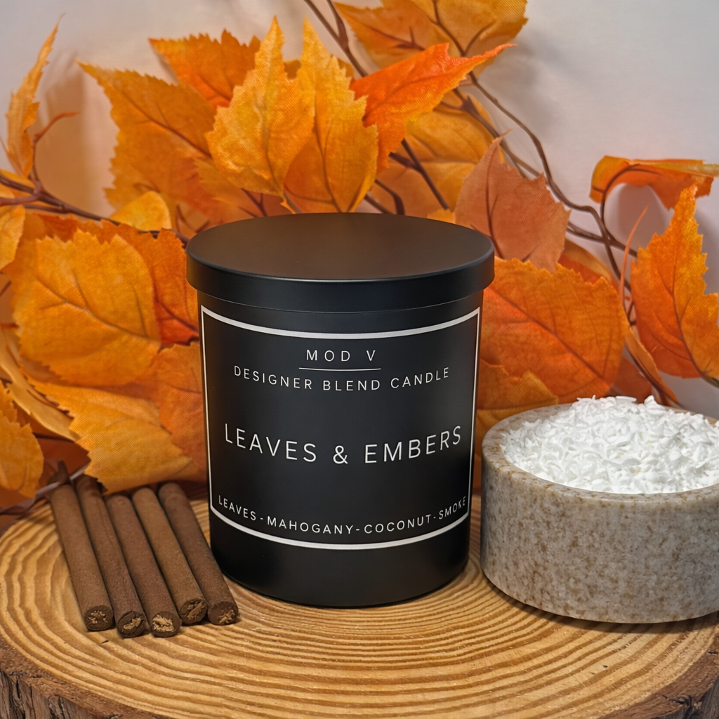 Candle labeled 'Leaves & Embers' with autumn leaves and cinnamon sticks on a wooden surface