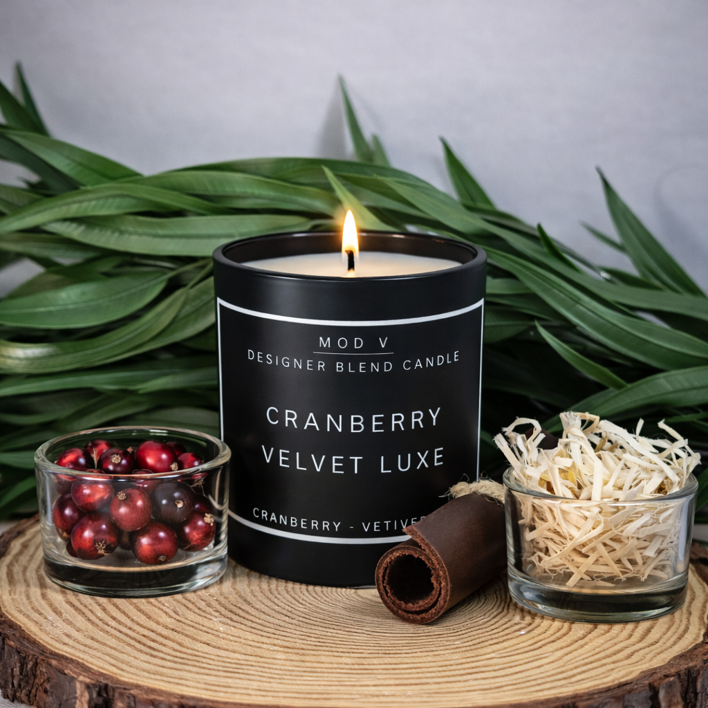 Candle labeled 'Cranberry Velvet Luxe' on a wooden surface with decorative items and greenery.