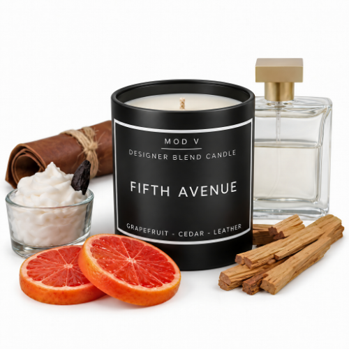 A black candle jar labeled 'FIFTH AVENUE' by MOD V, styled with grapefruit slices, cinnamon sticks, a small glass bowl of white wax, a rolled brown paper item, and a clear perfume bottle on a white background.