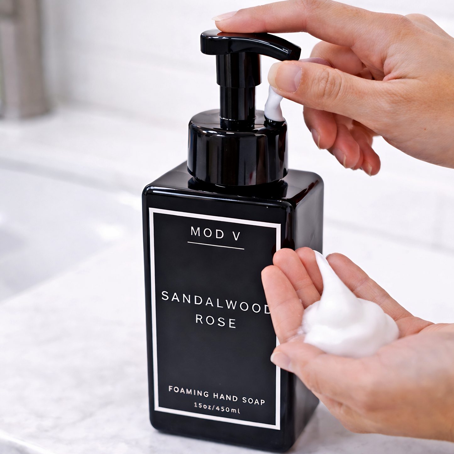 Black pump bottle of Sandalwood Rose foaming hand soap with a hand squeezing the pump.