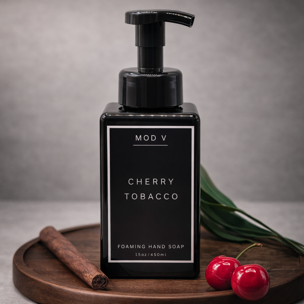 Black foaming hand soap bottle labeled 'MOD V Cherry Tobacco' on a wooden tray with cinnamon stick and cherries.