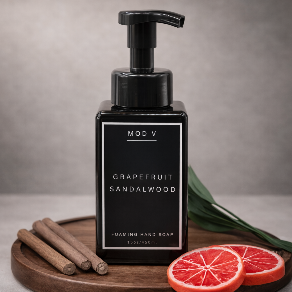 Black pump bottle of 'Mod V Grapefruit Sandalwood' foaming hand soap on a wooden tray with cinnamon sticks and grapefruit slices.