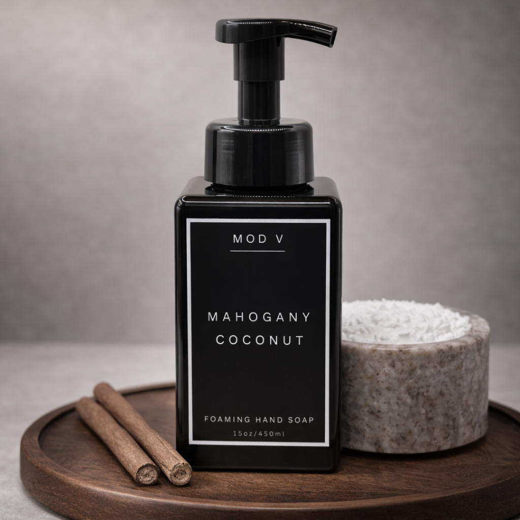 Black foaming hand soap bottle labeled 'MOD V Mahogany Coconut' on a wooden tray with a gray background.