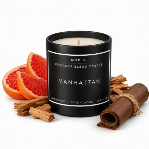 A black candle jar labeled 'MANHATTAN' by MOD V, styled with grapefruit slices, cinnamon sticks, and a leather roll on a white background.