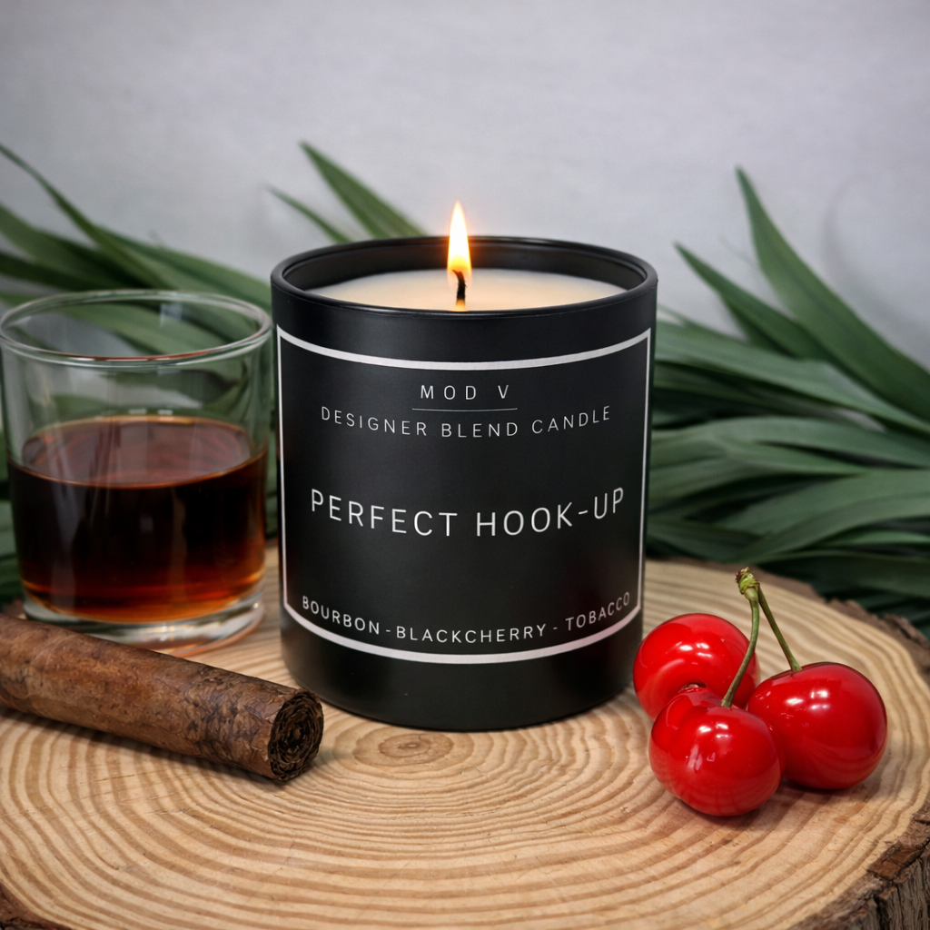 Candle labeled 'Perfect Hook-Up' with a glass of dark liquid, cinnamon stick, and cherries on a wooden surface.
