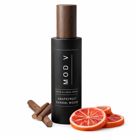 Black room & linen spray bottle with wooden cap, cinnamon sticks, and grapefruit slices on a white background