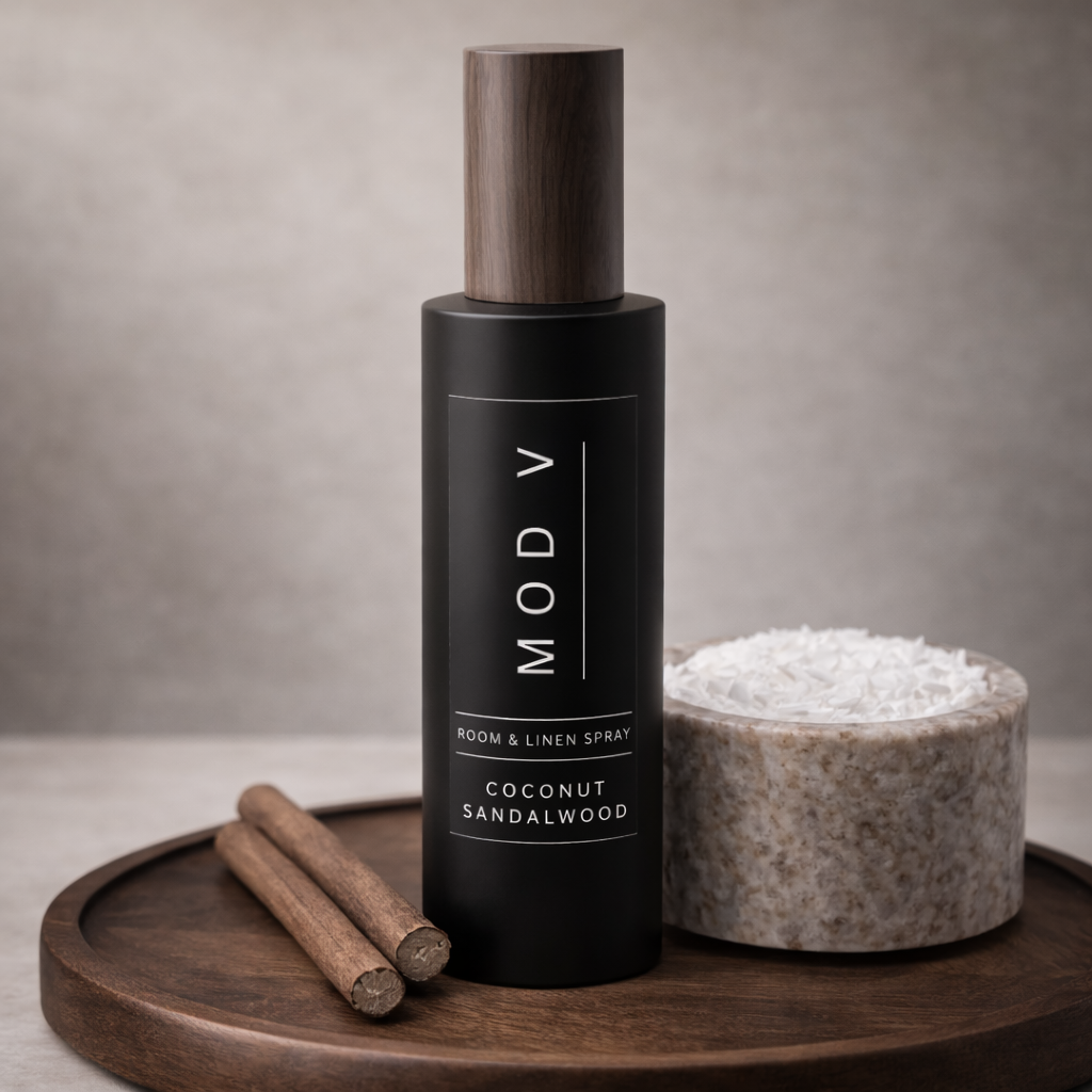 Black room & linen spray bottle labeled 'MODY' with wooden cap, cinnamon sticks, and a stone container on a wooden tray.