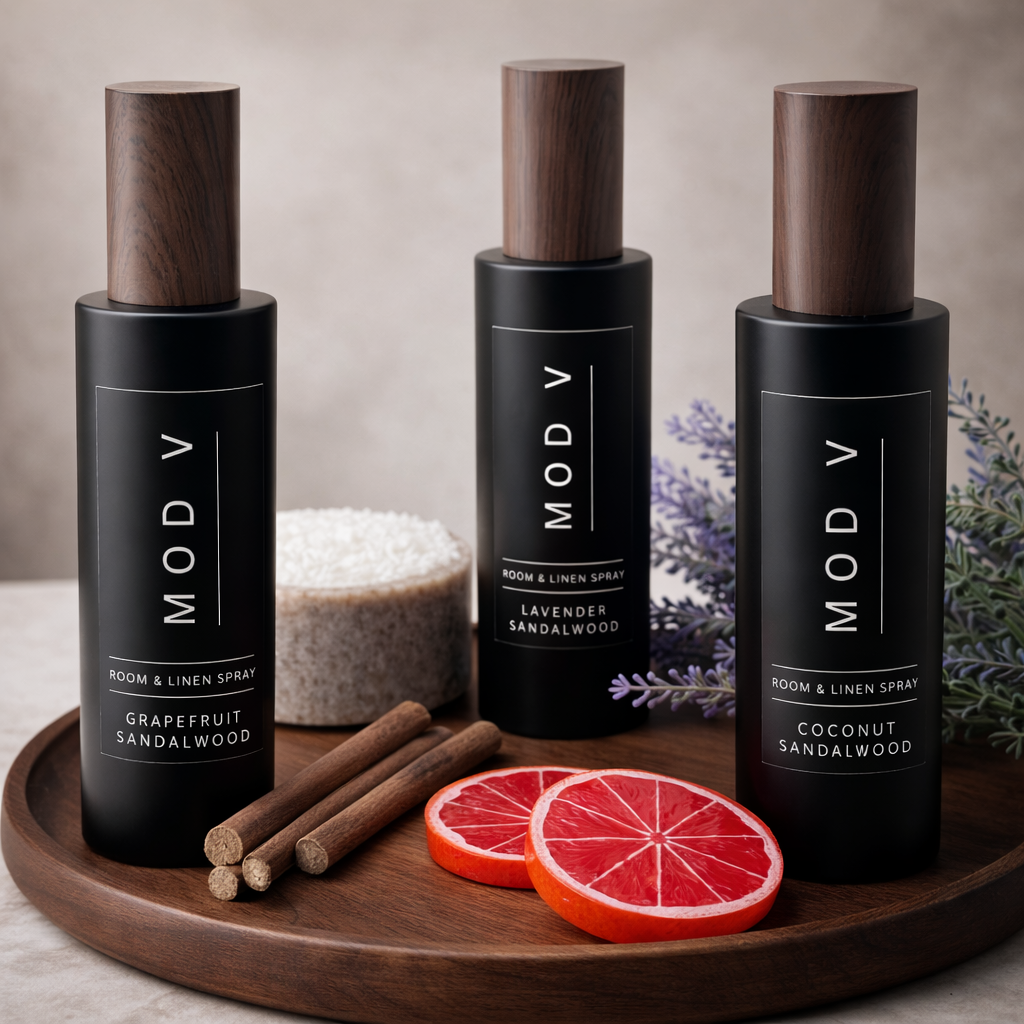 Three MOD V room & linen spray bottles on a wooden tray with citrus slices and cinnamon sticks.