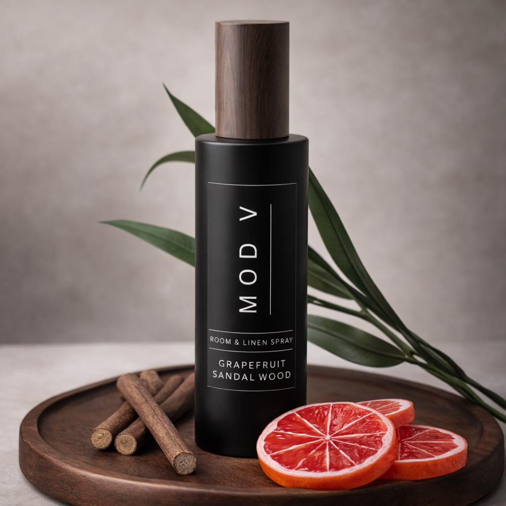 Black bottle of MOD V grapefruit sandalwood room spray on a wooden tray with cinnamon sticks and grapefruit slices.