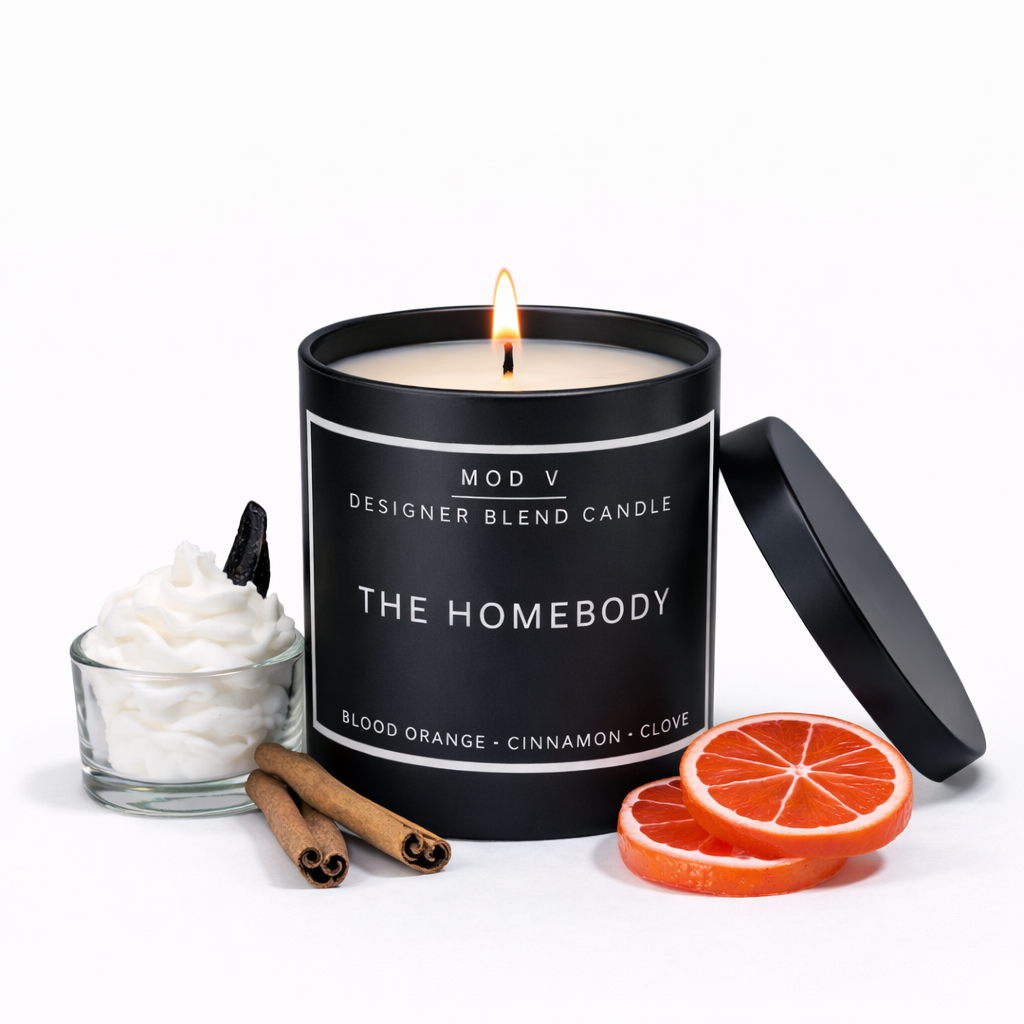 Designer blend candle with 'The Homebody' label, surrounded by orange slices, cinnamon sticks, and whipped cream on a white background.