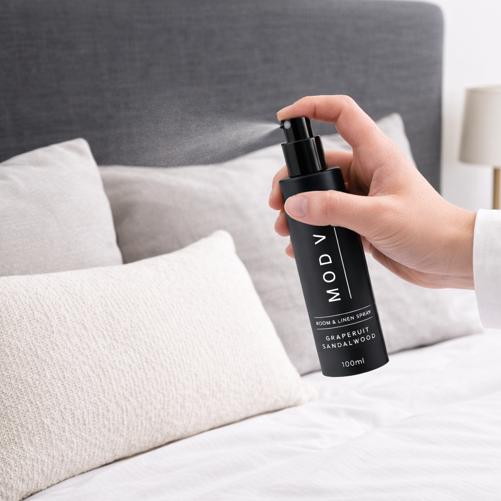 Hand holding a black Mody room spray bottle in a bedroom setting